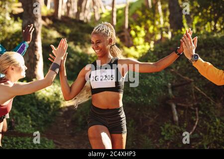 Felice arrivo del corridore maratona con gruppo di sostenitori al traguardo dopo la gara. Atleta femminile che dà i five alti ai tifosi in piedi a t. Foto Stock