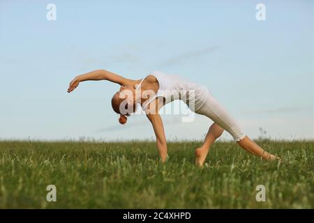 Equilibrio yoga in natura. Aggraziata giovane donna che pratica lo yoga backbend posa sul prato verde. Fit ragazza in piedi in posizione ponte all'aperto Foto Stock