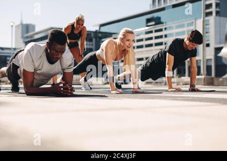 Gruppo di persone che fanno esercizio core su tappetino fitness all'aperto. Formazione di gruppo atletico insieme in città. Foto Stock