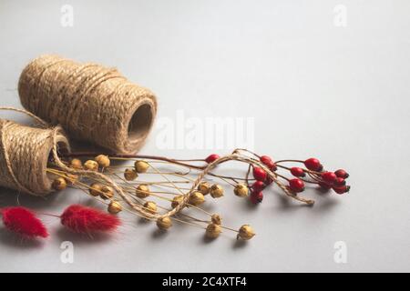 Composizione creativa con rotolo di spago di iuta naturale - lino o cannabis, con fiori secchi su sfondo chiaro con copyspace per il testo. Realizzati a mano e. Foto Stock