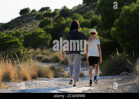 Madre e figlio camminano insieme in una foresta in una giornata di sole Foto Stock
