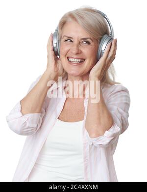 Bella donna bionda senior sta ascoltando musica in cuffie wireless isolate su sfondo bianco Foto Stock