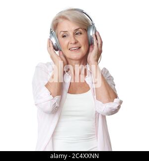 Bella donna bionda senior sta ascoltando musica in cuffie wireless isolate su sfondo bianco Foto Stock