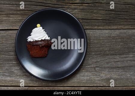 Una cupcake, sormontata con panna montata e decorata con una caramella a forma di bottone, è stata tagliata verticalmente e posta su una piastra su tavole di legno stagne. Foto Stock