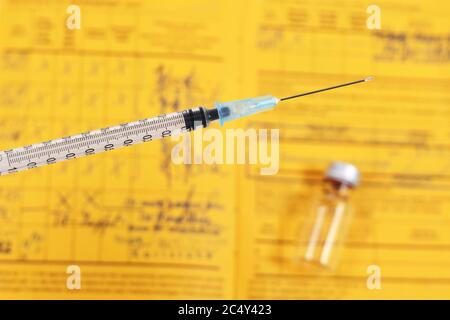 Concetto di vaccino con siringa davanti al flaconcino sfocato e certificato internazionale giallo di vaccinazione in background Foto Stock