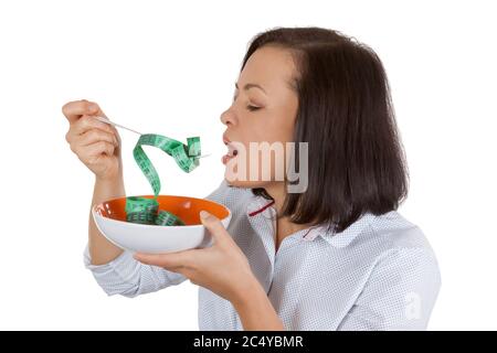 Perdita di peso e concetto di stile di vita sano. Fitness Donna cercando di mangiare nastro di misurazione su uno sfondo bianco Foto Stock