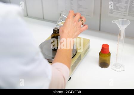 Un primo piano di una farmacista femminile che mescola liquidi chimici su bilance mediche in laboratorio Foto Stock