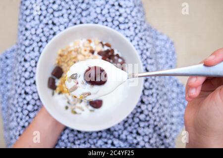 Donna irriconoscibile con cereali, yogurt, ciotola di frutta e cucchiaio a fuoco. Alimentazione sana, concetto di vita. Foto Stock