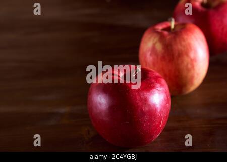 Tre mele rosse giacciono su un tavolo di legno alla cannella Foto Stock