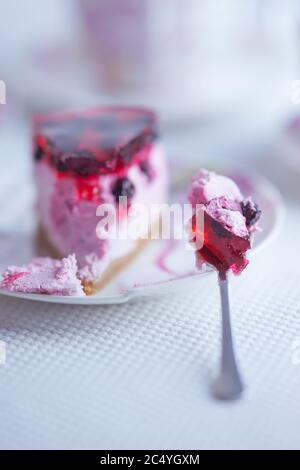 Una fetta di cheesecake al ribes rosso in un piattino con un cucchiaio su un tavolo bianco. Vista laterale. Foto Stock