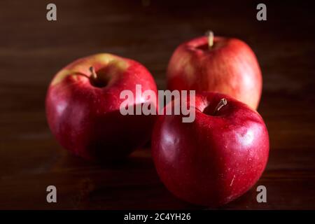 Tre mele rosse giacciono su un tavolo di legno alla cannella Foto Stock