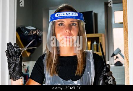 Donna parrucchiere che indossa DPI compreso uno scudo di guanti e grembiule preparazione per iniziare a lavorare di nuovo il 4 giugno 2020 come restrizioni di blocco sono attenuati in Inghilterra Foto Stock