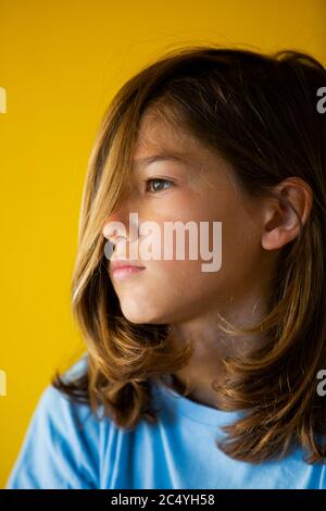 Ragazzo di undici anni con lunghi capelli biondi, con camicia blu, su sfondo giallo Foto Stock