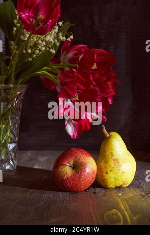 Tulipani rossi e lucertole in vaso e mela con pera su fondo nero Foto Stock