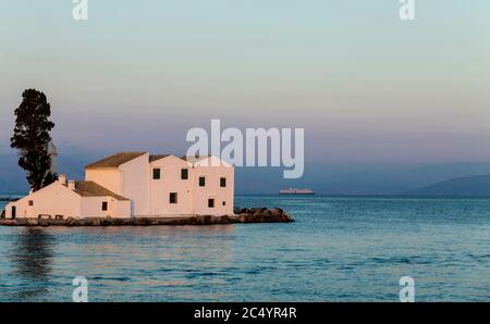 La chiesa di Panagia Vlacherna. Capo Kanoni, Corfù, Kerkyra, Grecia. Tramonto tranquillo, nave da crociera lontano all'orizzonte. Foto Stock