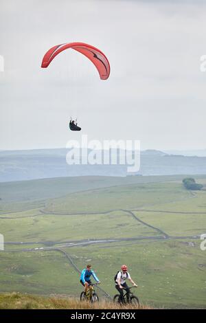 Parapendio al largo della collina di MAM Tor vicino a Castleton, nella vetta alta del Derbyshire, Inghilterra, mentre i ciclisti cavalcano lungo la cima Foto Stock