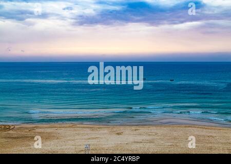 Tempo al tramonto e tramonto sulla spiaggia di Netanya, Israele, Mar Mediterraneo. Cielo, schiuma e onde. Vista aerea. 2 barche in mare. Foto Stock