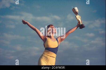 Giovane sportswoman bionda che guarda sulla Coppa del campione e che posa con il cielo di fondo. Indossa la parte superiore gialla e le leggins Foto Stock