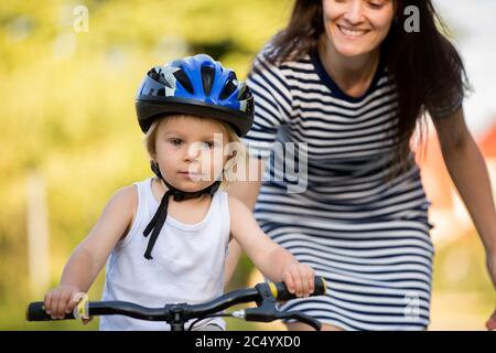 Giovane madre, aiutante suo figlio ad imparare a guidare una bicicletta, tenendolo e insegnandolo a andare in bicicletta Foto Stock