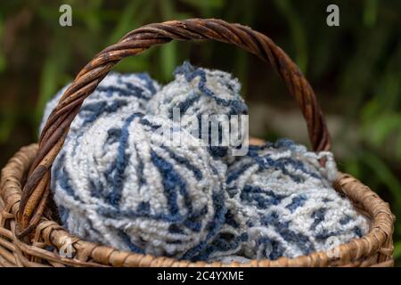Primo piano di palle di lana di filato bianco-blu su fondo naturale. Filato per maglieria. Articoli per agugliatrici femminili. Foto Stock