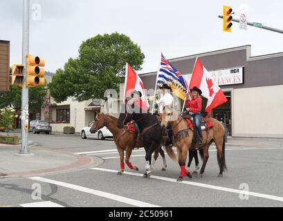 I motociclisti che portano bandiere canadesi e della British Columbia cavalcano i loro cavalli attraverso il centro di Williams Lake, British Columbia, Canada. I piloti erano celebrati Foto Stock
