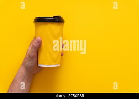 Caffè da andare in tazza di carta gialla nella mano sinistra caucasica su sfondo giallo, Foto Stock