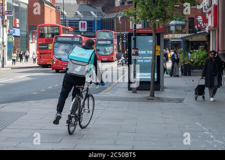 Un ciclista che lavora per il servizio di consegna a domicilio Deliveroo in una strada principale di Londra. Foto Stock