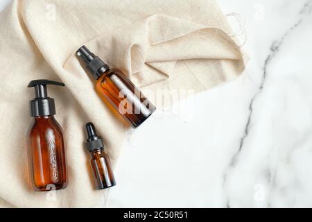 Bottiglie di vetro marrone ambrato con cosmetici biologici e tessuto beige su sfondo marmoreo. Mockup di prodotti di bellezza. Concetto di cura della pelle, trattamento del corpo. FLA Foto Stock