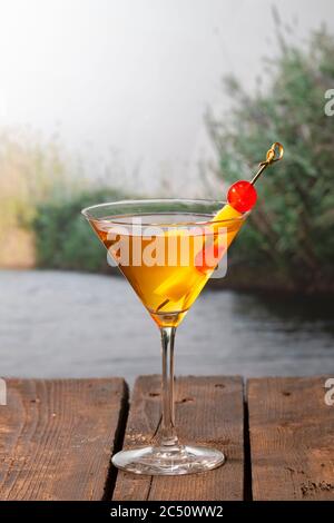 Primo piano di un cocktail dall'aspetto delizioso con uno spiedino con ciliegie e ananas a pezzetti su un tavolo di legno su uno sfondo fuori fuoco. Vacanze e l Foto Stock