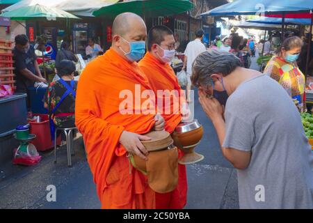 Due monaci buddisti che indossano maschere anti-Covid sono accolti con riverenza durante il loro giro giornaliero di elemosina (binta baat) in un mercato a Bangkok, Thailandia Foto Stock