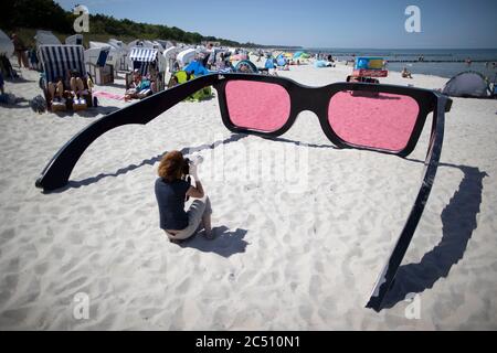 Zingst, Germania. 24 Giugno 2020. Un turista scatta una fotografia dei grandi vetri rosa di Marc Moser dal titolo "Sea Pink II", una mostra al festival fotografico "Horizonte" del 2016, sulla spiaggia del Mar Baltico. Con il sole e temperature intorno ai 25 gradi, molti turisti usano il tempo estivo per una giornata in spiaggia. Credit: Jens Büttner/dpa-Zentralbild/ZB/dpa/Alamy Live News Foto Stock