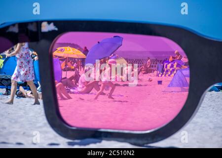 Zingst, Germania. 24 Giugno 2020. I grandi vetri rosa con il titolo 'Sea Pink II' di Marc Moser, mostra del festival fotografico 'Horizonte' 2016, sulla spiaggia del Mar Baltico. Con il sole e temperature intorno ai 25 gradi, molti turisti usano il tempo estivo per una giornata in spiaggia. Gli alberghi, le pensioni e i campeggi nelle regioni turistiche del Meclemburgo-Vorpommern sono attualmente molto ben utilizzati. Credit: Jens Büttner/dpa-Zentralbild/ZB/dpa/Alamy Live News Foto Stock