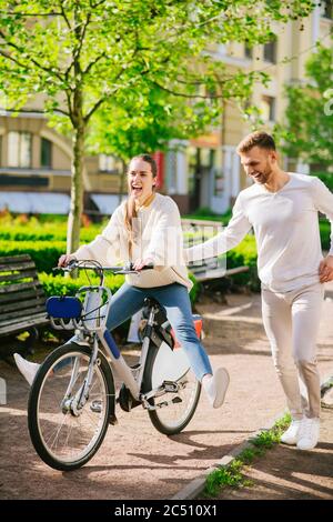 Donna allegra in bicicletta e uomo attento che corre nelle vicinanze Foto Stock