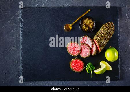 salame rivestito con pepe verde intero e hanno affettato su una tavola di pietra nera e servito con pesto al basilico e zeppe di lime, piatto, primo piano, ho Foto Stock