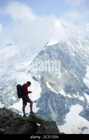 Silhouette di uomo in piedi su rocce nelle Alpi Pennine in Svizzera. Viaggiatore con gps navigatore tracker alla ricerca di coordinate, incredibile Monte Ober Gabelhorn leggermente in nuvole è sullo sfondo Foto Stock