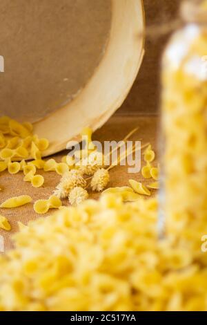 Pasta in un vaso, molta pasta è sparsa intorno, un vaso si trova su un supporto di legno Foto Stock