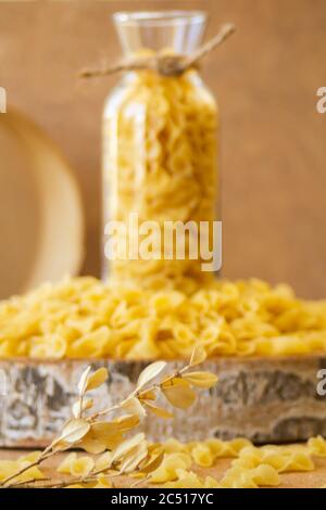 Pasta in un vaso, molta pasta è sparsa intorno, un vaso si trova su un supporto di legno Foto Stock