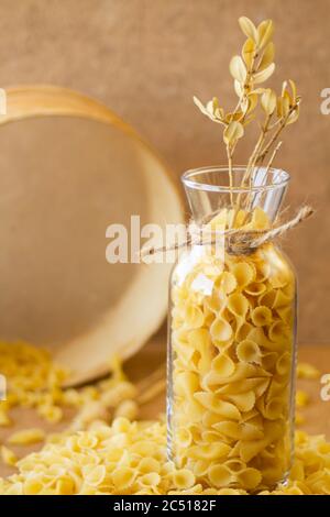 Pasta in un vaso, molta pasta è sparsa intorno, un vaso si trova su un supporto di legno Foto Stock