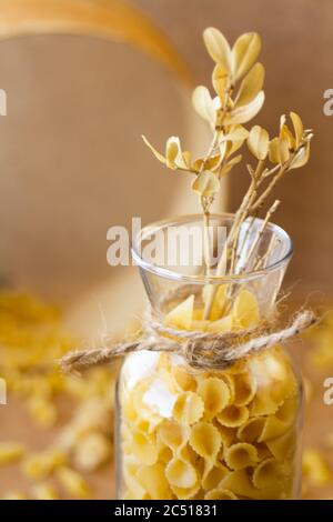 Pasta in un vaso, molta pasta è sparsa intorno, un vaso si trova su un supporto di legno Foto Stock