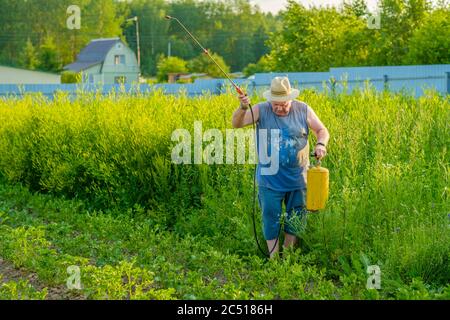 Un uomo anziano in un cappello spruzzi un insetticida sulle cime delle patate. La lotta contro il coleottero di patate del Colorado e altri insetti nocivi. Estate Foto Stock