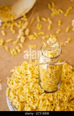 Pasta in un vaso, molta pasta è sparsa intorno, un vaso si trova su un supporto di legno Foto Stock