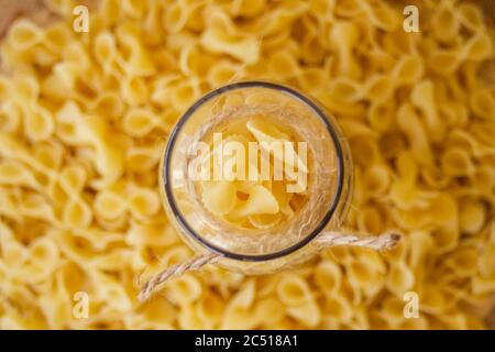 Pasta in un vaso, molta pasta è sparsa intorno, un vaso si trova su un supporto di legno Foto Stock