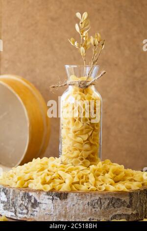 Pasta in un vaso, molta pasta è sparsa intorno, un vaso si trova su un supporto di legno Foto Stock