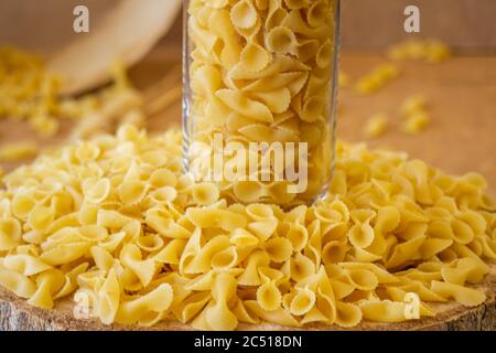 Pasta in un vaso, molta pasta è sparsa intorno, un vaso si trova su un supporto di legno Foto Stock