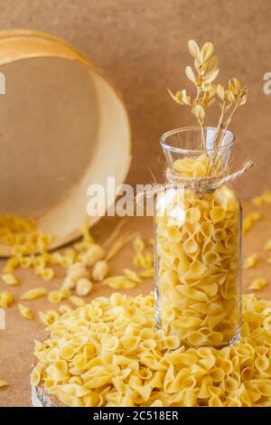 Pasta in un vaso, molta pasta è sparsa intorno, un vaso si trova su un supporto di legno Foto Stock