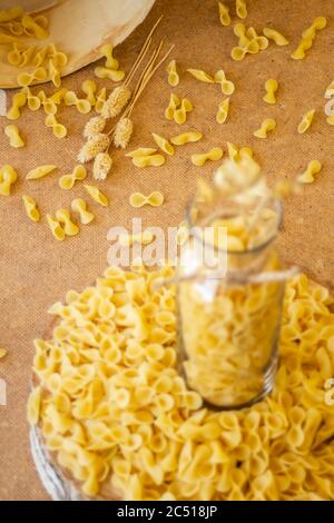 Pasta in un vaso, molta pasta è sparsa intorno, un vaso si trova su un supporto di legno Foto Stock