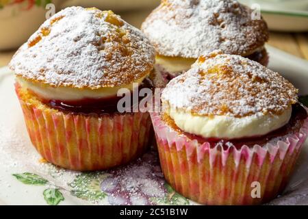 Un primo piano di tre Cupcakes con crema e marmellata su un piatto laterale Foto Stock