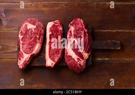 Varietà di freschi Black Angus prime carne di manzo: ribeye, striploin e picanha su tavoletta di legno sfondo copia spazio vista dall'alto Foto Stock