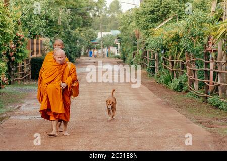 31 MAGGIO 2018 SA Kaeo, Thailandia - Monaci Buddisti tailandesi camminano lungo la tranquilla strada del villaggio per le elemosine mattutine seguite da un cane di strada Foto Stock