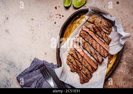 Bistecca di manzo alla griglia a fette con spezie in un piatto scuro, sfondo scuro. Foto Stock